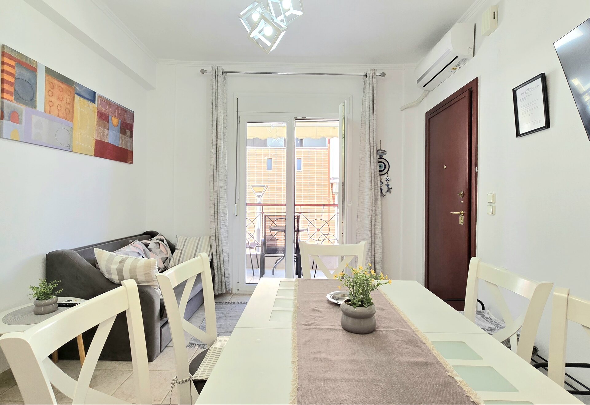 Polychrono Two Bedroom Apartment living room with dining table, sofa, TV, and balcony door